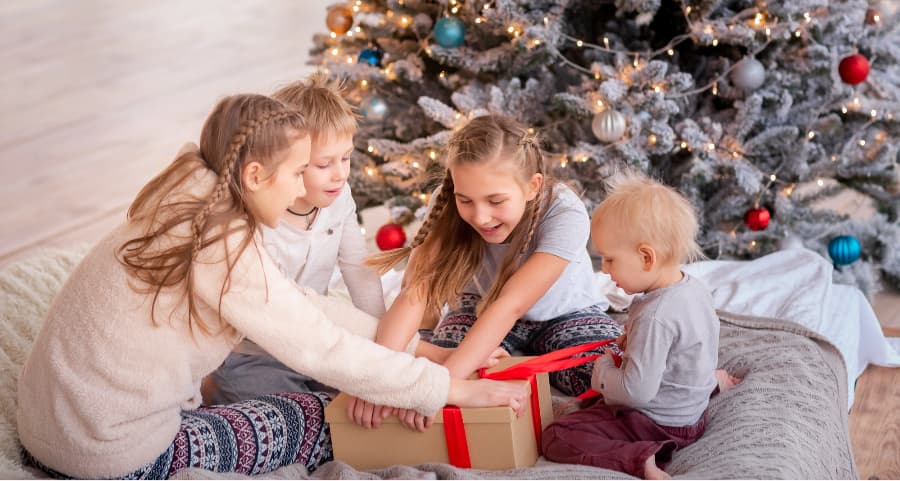 Kids opening a present in the living room next to a Christmas tree.